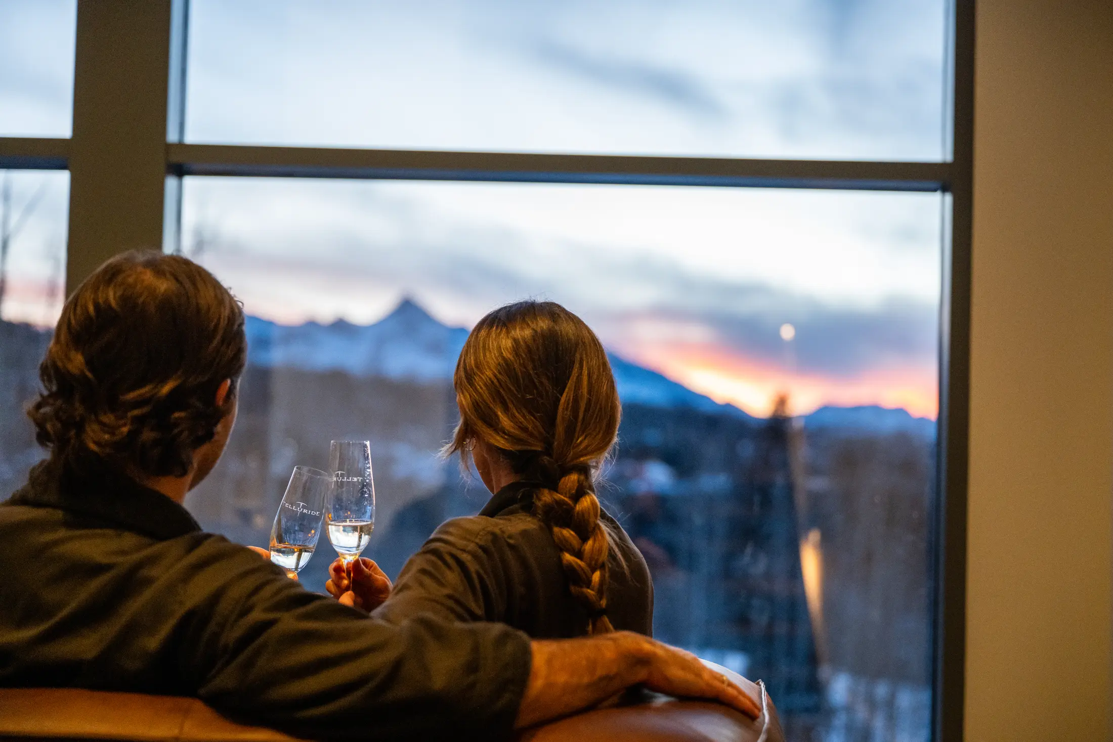 A couple in spa robes toast with Telluride wine glasses while watching the sunset over the San Juan Mountains