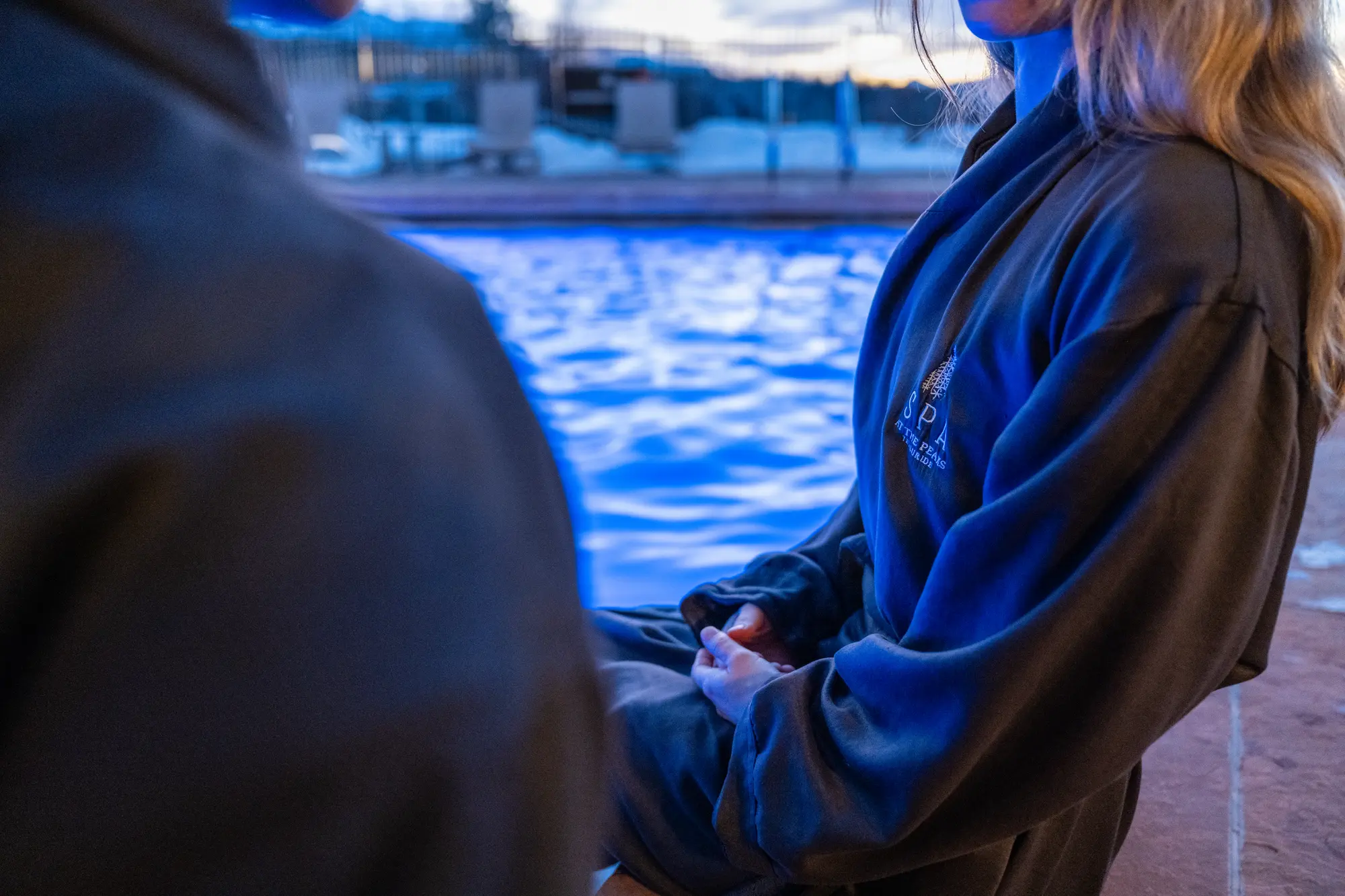 A guest in a spa robe relaxes beside the outdoor pool